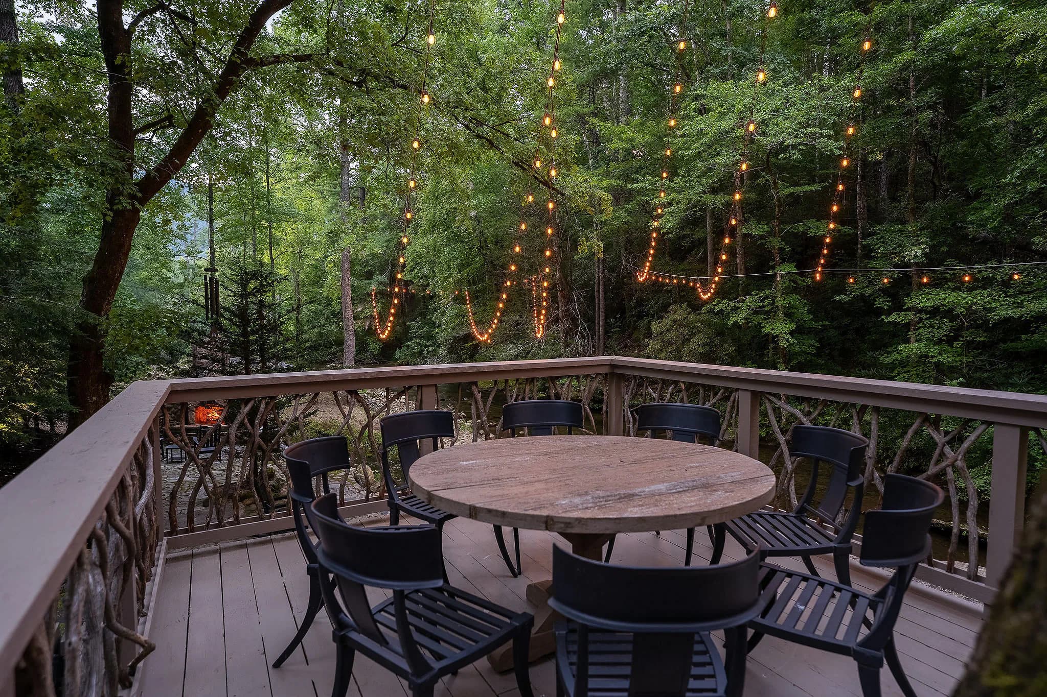 Deck dining table under string lights at dusk at a riverfront cabin near Greenville SC