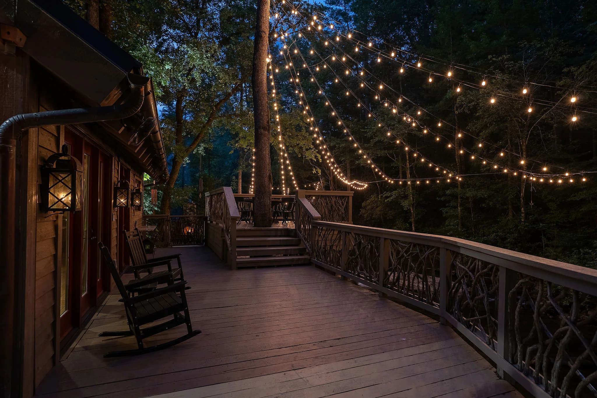 Rocking chairs on a deck with handcrafted branch railings and string lights at a Marietta SC river cabin