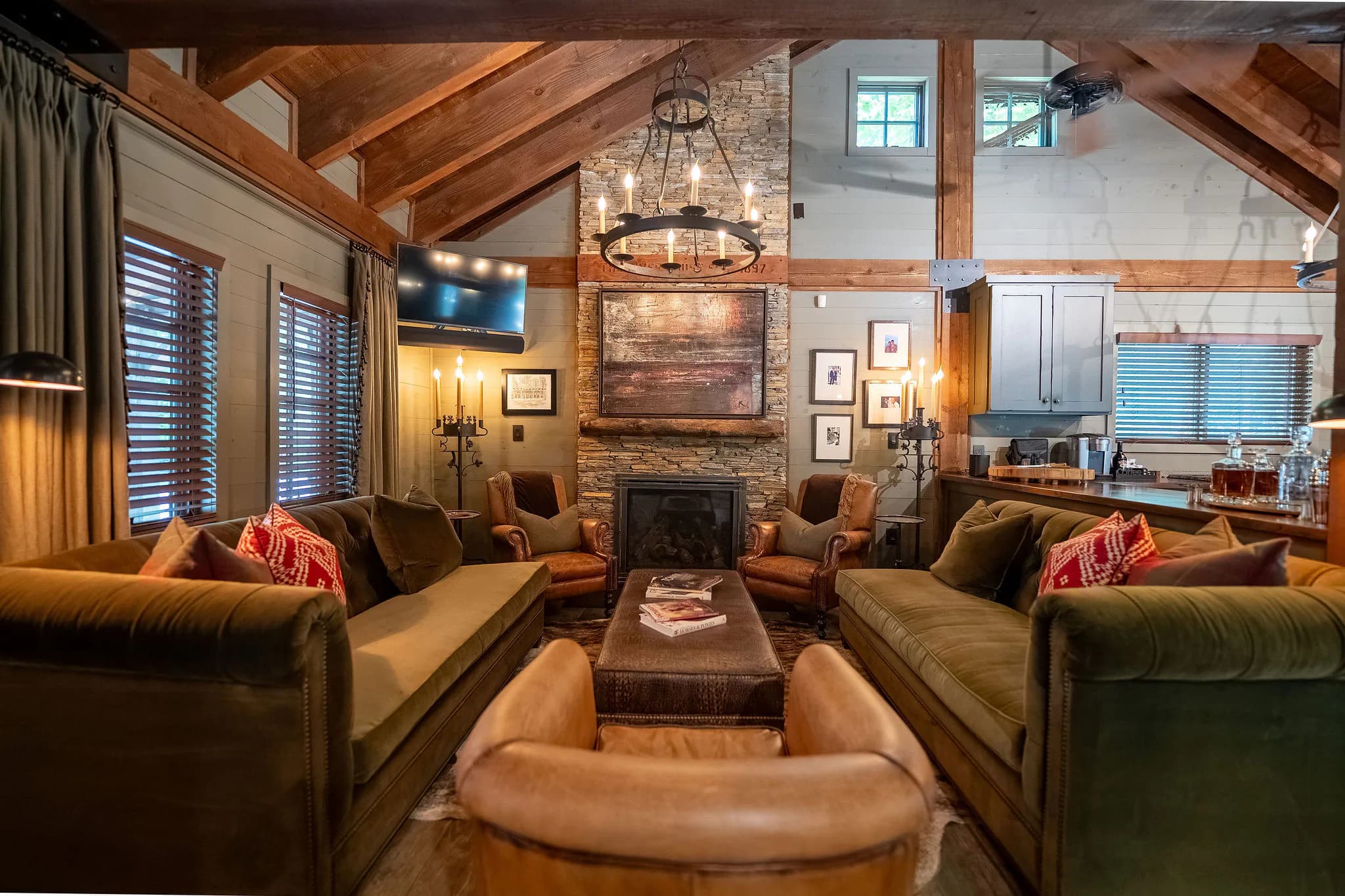 Great room with vaulted timber beams, a stone fireplace and leather club chairs in a Marietta SC cabin