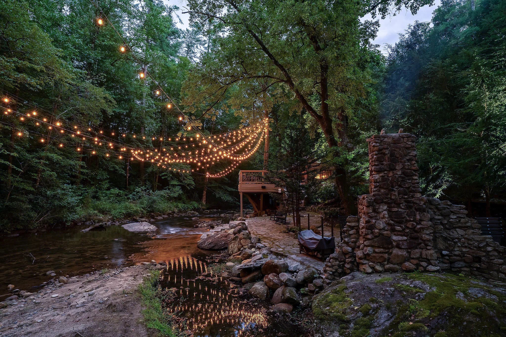String lights reflected in the Middle Saluda River beside a stone chimney fireplace near Jones Gap State Park