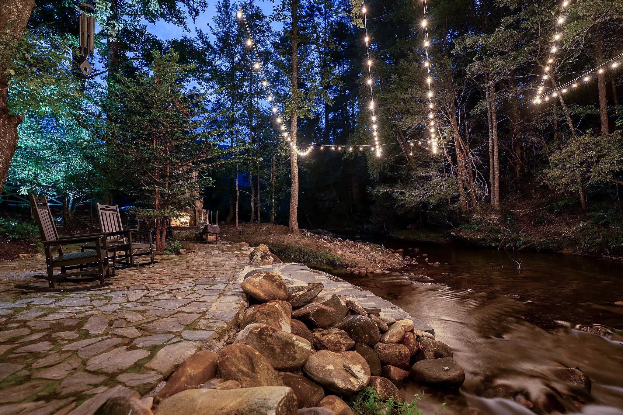 String lights over the Middle Saluda River at blue hour beside the stone patio of a Jones Gap cabin rental
