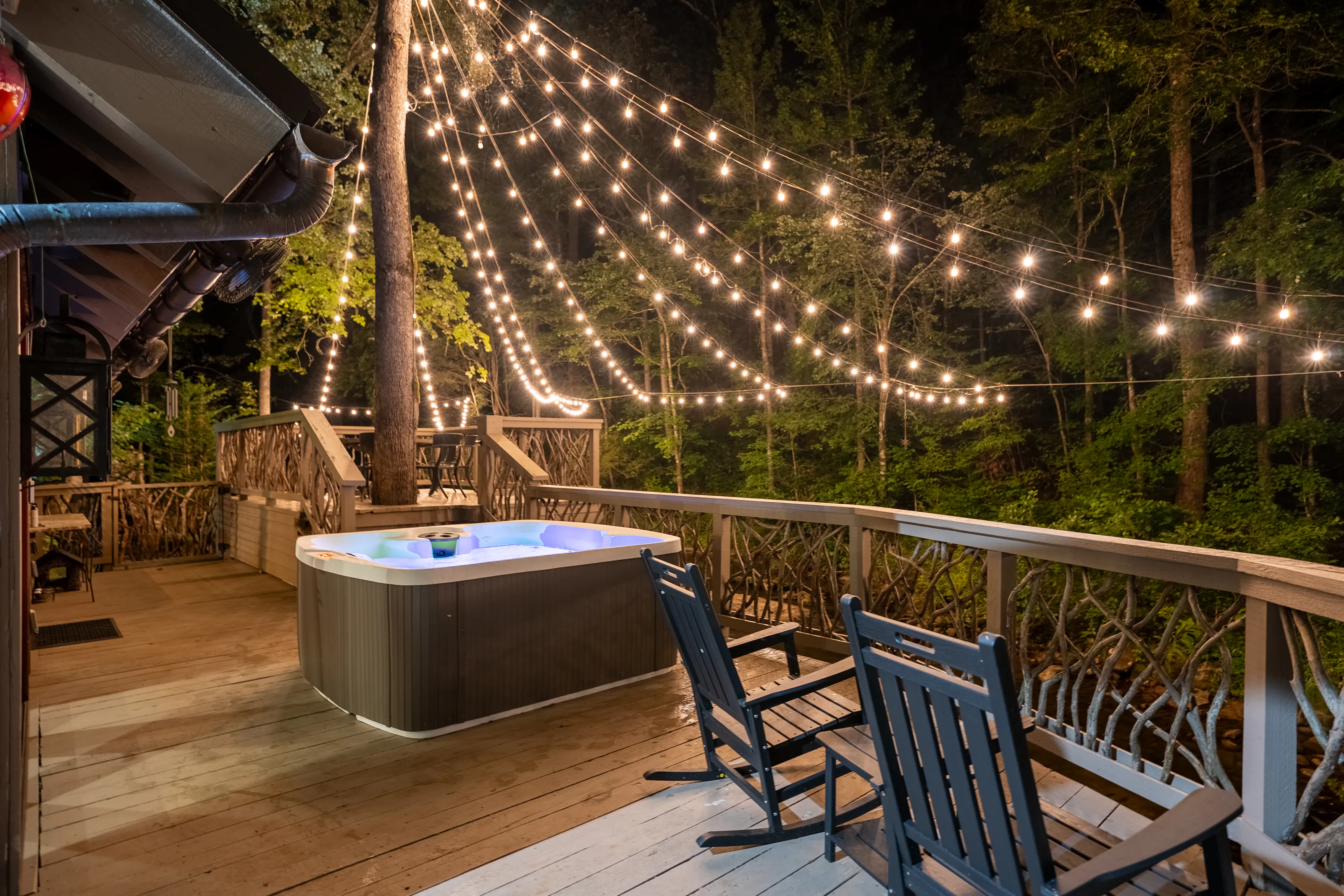 Hot tub glowing under a canopy of string lights on the riverfront deck at night